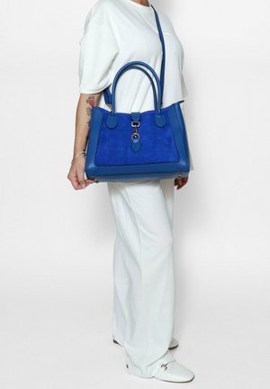 Sac à main bleu avec un mélange de textures lisses et en suède, présentant deux poignées arrondies, une bandoulière amovible et des détails de couture contrastés.