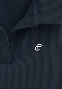 Marinblå ribbad polo skjorta med vikbar krage och vit broderad logotyp på bröstet. Tyget har en texturerad yta.