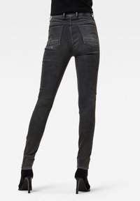 Jeans skinny negros con una textura suave, que cuentan con dos bolsillos traseros y una cintura de altura media, combinados con zapatos de tacón altos negros.