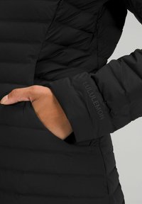 Crna izolirana jakna s kvadratnim uzorkom i bočnim džepom. Na manžetama se nalazi diskretni Lululemon logo u usklađenoj boji.