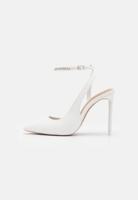 Chaussure à talon haut blanche, à bride arrière, avec un bout pointu, une tige en synthétique lisse, une sangle de cheville ajustable ornée de strass et un fin talon stiletto.