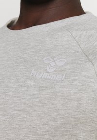 Sweat-shirt gris clair en tissu texturé, avec un logo "hummel" en relief subtil et un col rond.