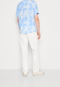 Kortärmad, ljusblå batiktröja i kombination med vita byxor och beige sneakers, med en avslappnad passform och mjuk textur.