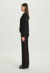 Pull en laine noir et pantalon avec une bande latérale rouge. L'ensemble a une coupe décontractée et une texture lisse, avec un cordon de serrage sur le pantalon.