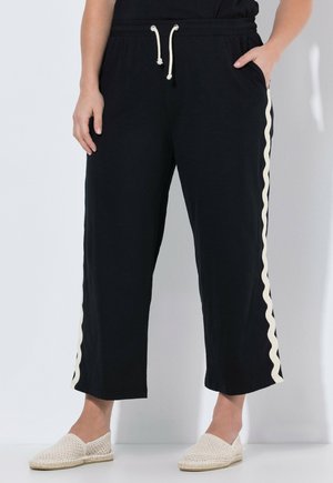 Sorte vidde-bukser med hvide bølgede sidestriber, elastisk talje med snøre, båret med beige vævede slip-on sko.