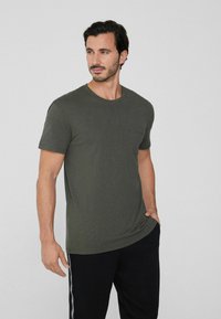 Oliwkowa koszulka z okrągłym dekoltem, krótkimi rękawami i kieszonką na piersi. Materiał wydaje się być miękki z lekko teksturowanym wykończeniem.