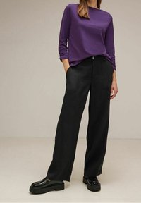 Lila långärmad skjorta i kombination med vida svarta byxor och kraftiga svarta loafers. Släta texturer, kontrast mellan färger.