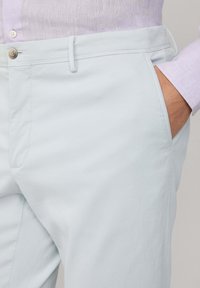 Hellblaue Hosen mit glatter Textur, ausgestattet mit einem Knopfverschluss, Gürtel-Schlaufen und Seitentaschen. Der Stoff wirkt leicht und atmungsaktiv.