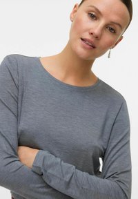 Maglia grigia a maniche lunghe con scollo rotondo e maniche aderenti, realizzata in un tessuto morbido e leggero con una texture liscia.