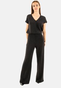 Jumpsuit noir à col en V, à manches courtes et avec une coupe évasée. Fabriqué en tissu texturé et scintillant, il présente une coupe décontractée et un style minimaliste.
