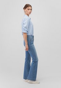 Hellblaues Hemd mit aufgerollten Ärmeln, kombiniert mit ausgestellten blauen Jeans und weißen Turnschuhen. Es hat eine schmale Passform und einen leichten Verwaschungseffekt.