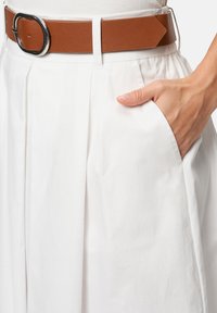 Weißer plissierter Rock mit seitlichen Taschen, kombiniert mit einem braunen strukturierten Leder-Gürtel mit einer silbernen runden Schnalle.