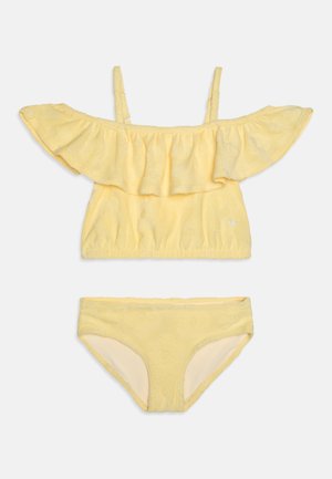To-delt bikini i lys gul. Toppen har off-shoulder flæser og et struktureret blomstermønster; bukserne har matchende blomstermotiv.