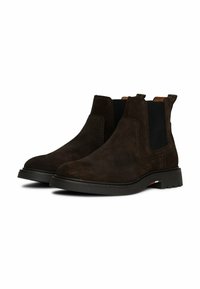 Stivali Chelsea in suede marrone con pannelli elastici laterali, punta rotonda e suola in gomma nera a contrasto. Dettagli di cucitura minimi.
