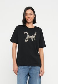 Μαύρο βαμβακερό μπλουζάκι με μεγάλο ασημένιο παγιετένιο σχέδιο "Good!" στο στήθος. Άνετη εφαρμογή με κοντά μανίκια και στρογγυλή λαιμόκοψη.