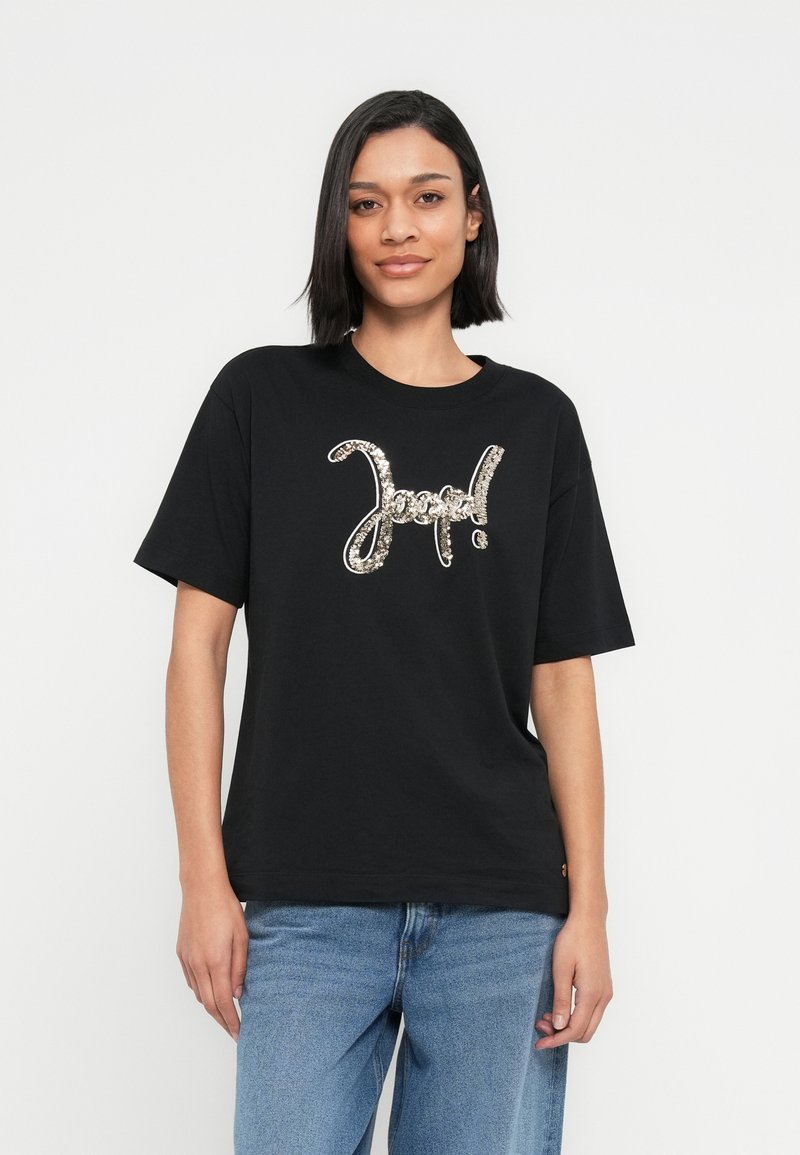 Μαύρο βαμβακερό μπλουζάκι με μεγάλο ασημένιο παγιετένιο σχέδιο "Good!" στο στήθος. Άνετη εφαρμογή με κοντά μανίκια και στρογγυλή λαιμόκοψη.