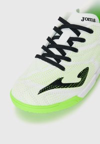 Scarpa sportiva bianca con lacci neri, accenti verdi e tomaia testurizzata caratterizzata da un motivo di piccole perforazioni e un logo nero.