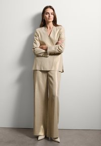 Completo tre pezzi in metallo dorato composto da un blazer su misura, pantaloni a gamba larga e décolleté a punta, caratterizzato da una texture liscia.