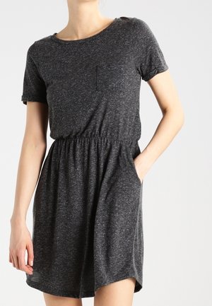 Frau trägt ein dunkelgraues, kurzärmeliges Freizeitkleid mit elastischem Taillenbund und Seitentaschen, steht vor einem schlichten hellen Hintergrund.