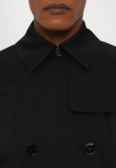 Manteau noir en trench avec un large col, design croisé et boutons brillants. Texture lisse, lignes épurées et esthétique moderne.