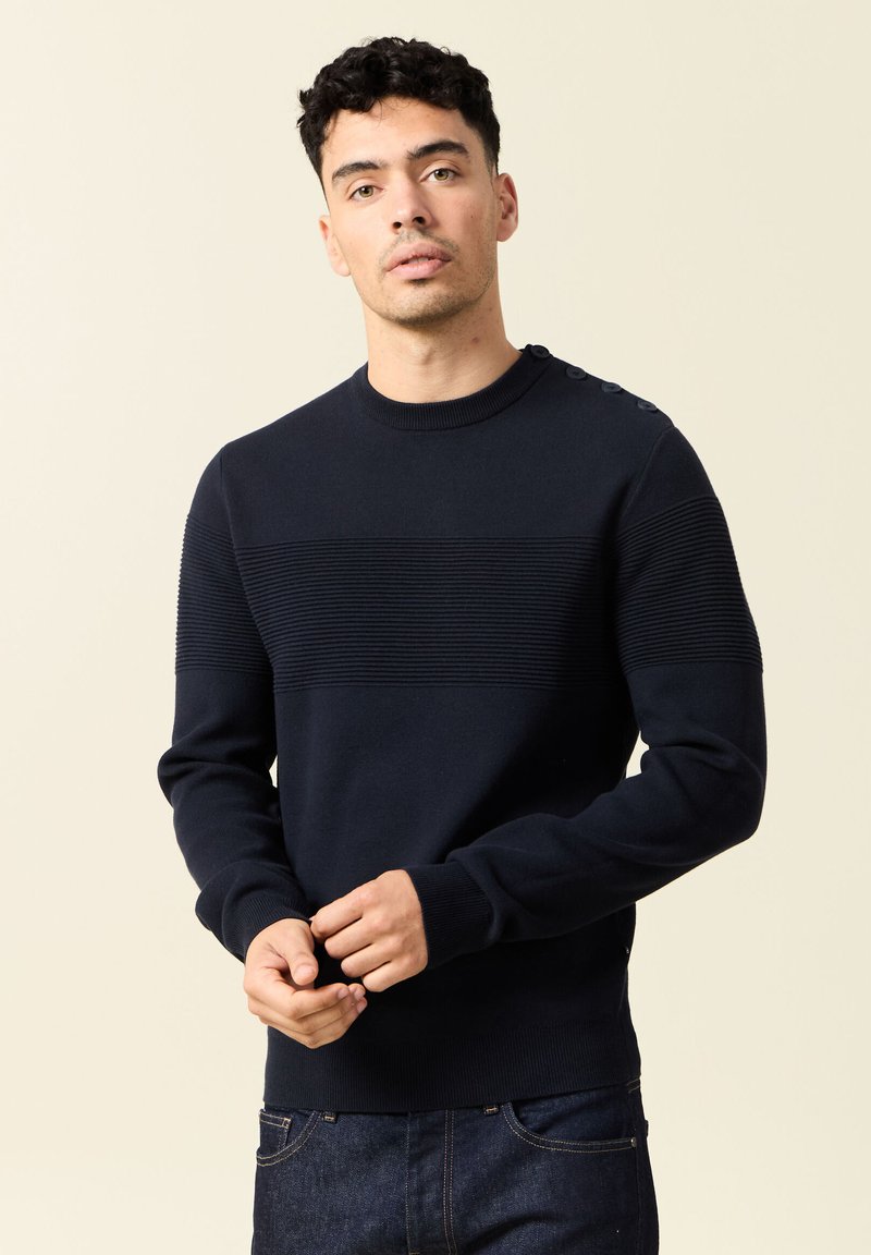 Maglione a maglia blu navy con texture a righe orizzontali, scollatura rotonda e dettagli con bottoni sulle spalle. Tessuto morbido.