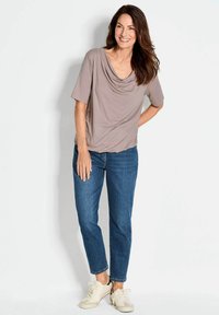 Lichtbruine draperende top met korte mouwen, gecombineerd met blauwe jeans en beige sneakers. De top heeft een zachte, gladde textuur.