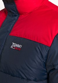 Röd och marinblå puffjacka med hög krage, tryckknappar och broderad Tommy Jeans-logotyp på bröstet.