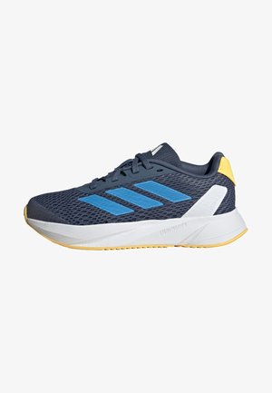 Zapatilla deportiva en color navy con parte superior de malla, rayas azules, una media suela blanca y detalles amarillos en el talón. Cuenta con una suela de goma para mayor tracción.