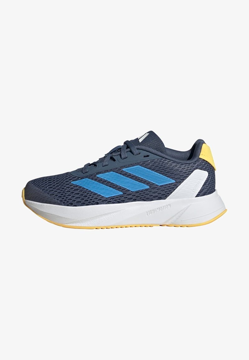 Zapatilla deportiva en color navy con parte superior de malla, rayas azules, una media suela blanca y detalles amarillos en el talón. Cuenta con una suela de goma para mayor tracción.