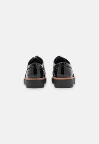 Scarpe in pelle verniciata nera con dettagli brogue, tacco corto e un accento in pelle marrone lungo la suola. Finitura liscia e lucida.