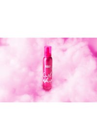 Roze metalen spuitfles met een pompdeksel, gelabeld "Curl Whip," rustend op een roze pluizige achtergrond. Product voor het activeren van krullen.