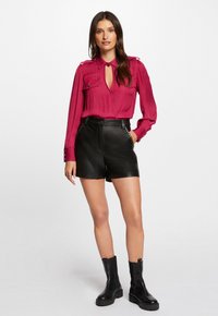 Fuchsia bluse med nøglehul-neckline og dobbelt brystlomme, parret med højtaljede sorte lædershorts og kraftige sorte ankelstøvler.