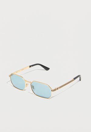 Solbriller med gullramme, lyseblå oktagonale linser og svarte tempeltupper, med gresk nøkkelmønster på armene.