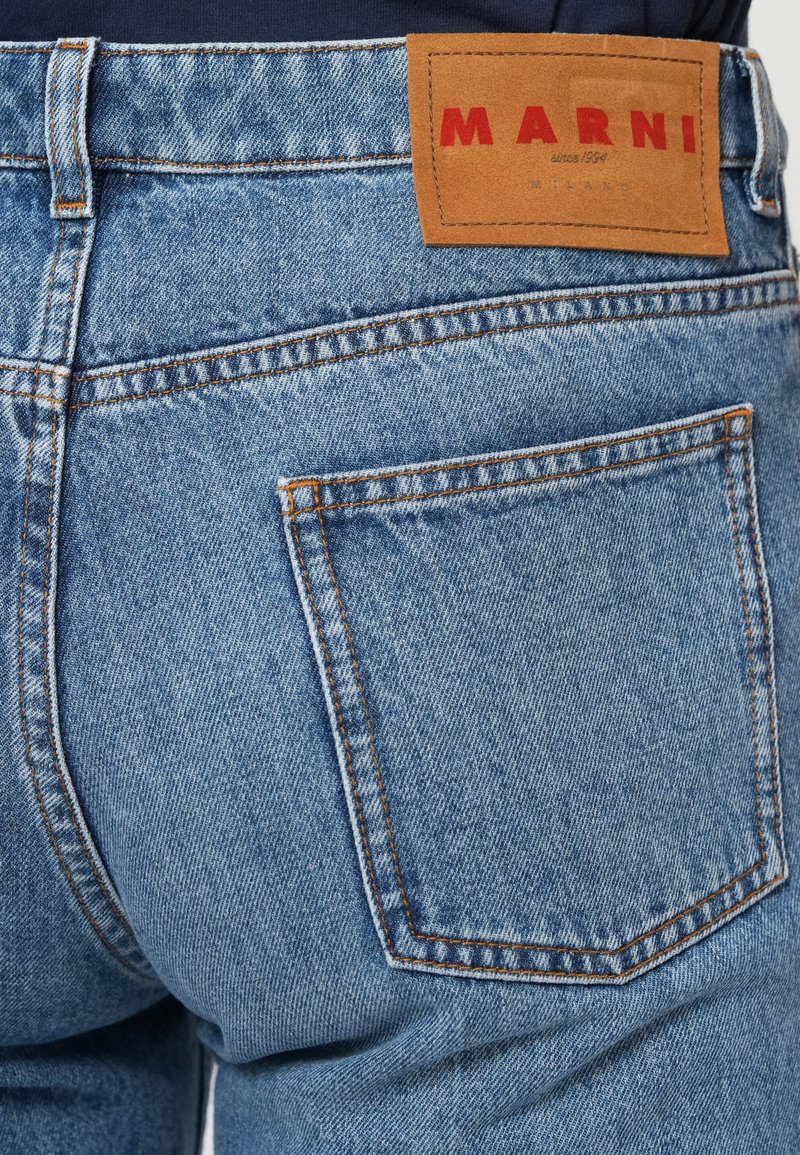 Blaue Jeans, Rückansicht, mit einem braunen Lederschild, auf dem in roter Schrift "MARNI" steht, und orangefarbenen Nähten.