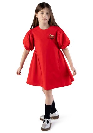 Rode katoenen jurk met pofmouwen en zijsamenspel. Voorzijde met een paardenafbeelding. Gecombineerd met zwarte sokken en zilveren schoenen.