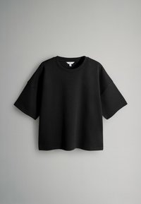 Melnā pārspīlētā T-krekla no kokvilnas maisījuma, ar apaļu kakla izgriezumu, īsām piedurknēm un brīvu piegriezumu ar gludu, matētu virsmu.