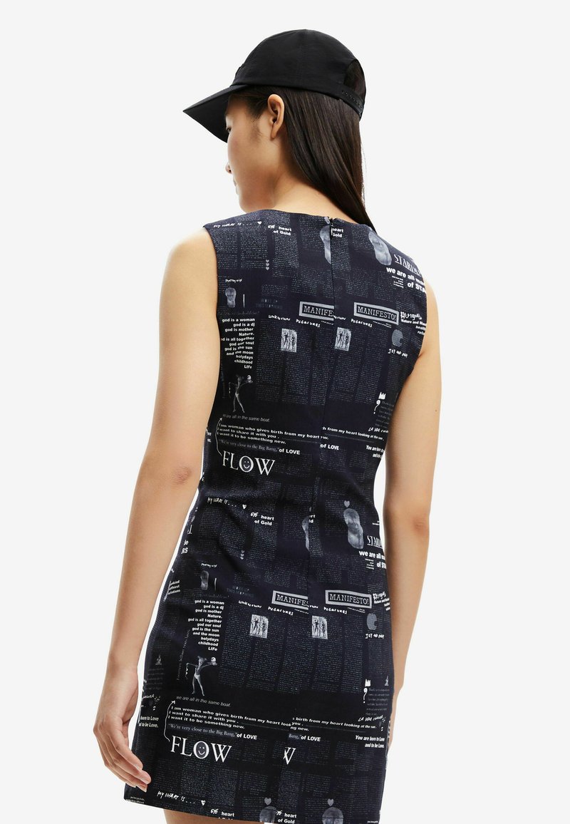 Femme portant une robe sans manches noire avec des textes et des graphiques blancs, et une casquette de baseball noire, vue de dos.