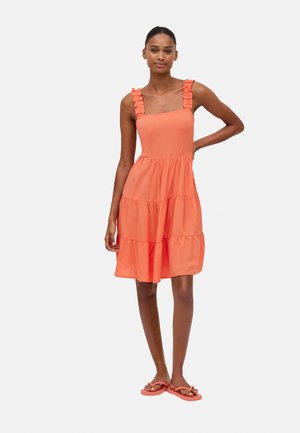 Orange gestufktes Kleid mit Rüschenträgern, einem Quadrat-Ausschnitt und einem fließenden Rock. Getragen von einem Model mit passenden Flip-Flops.