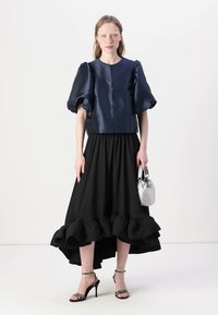 Marine satin cropped topp med pufferm, sammen med et svart maxiskjørt med volangkant. Sølvveske og spisse hæler.