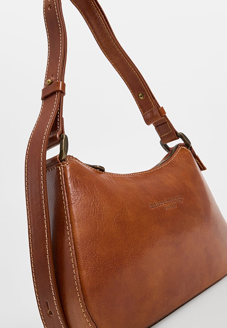 Braune Lederhandtasche mit geschwungener Form, verstellbarem Trageriemen und sichtbaren Nähten. Hat eine geprägte Logodetail und antike Hardware-Akzente.