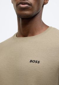 Μπεζ πλεκτό φούτερ με υφή υφάσματος και μαύρο κεντημένο λογότυπο "BOSS" στο στήθος. Στρογγυλή λαιμόκοψη, casual εφαρμογή.