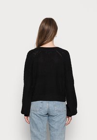 Svart kortklippt tröja med strukturerad stickning, med flätstickade detaljer på ärmarna och ribbad fåll. Bärs med ljusblå jeans.