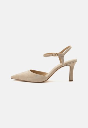 Beige ruskind højhælet sko med spids tå, ankelrem og guldlås, vist på en ensfarvet hvid baggrund.