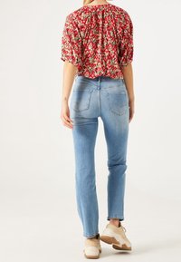 Red floral blouse with a gathered back, paired with light blue fitted jeans and beige sneakers, showcasing a casual outfit.