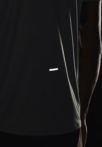 Czarna odzież sportowa o smukłym designie, z odblaskowym paskiem z tyłu i gładką fakturą tkaniny. Krótkie rękawy, luźny krój.