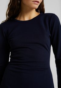 Laivastonsininen pitkähihaisen paita, joka on tehty sileästä kankaasta ja jossa on istuva siluetti, pyöreä pääntie ja vähäiset saumalinnit.