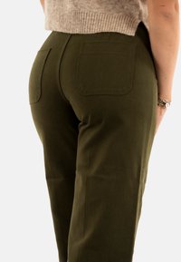 Pantalons larges verts foncés avec deux poches arrière, texture lisse et taille mi-haute. Présente des détails de couture subtils.