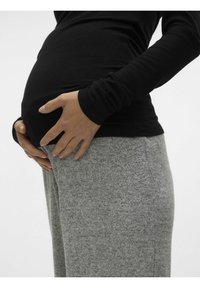 Črna rebrasta dolgosleeve majica prek sive, mehke tkanine, prilegajoče hlače. Roka se naslanja na vidni nosečniški trebuh, kar poudarja okroglo obliko.