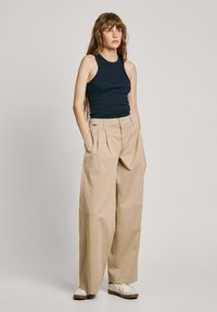 Débardeur marine associé à un pantalon large taille haute beige. Le pantalon possède des plissés et des poches, et est composé d'un tissu lisse.