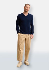 Marinblå v-halströja, mjukt tyg, passformade ärmar. Beige avsmalnande byxor, lätt material, uppvikta nederdelar. Beiga skor, tjock sula med snörning.